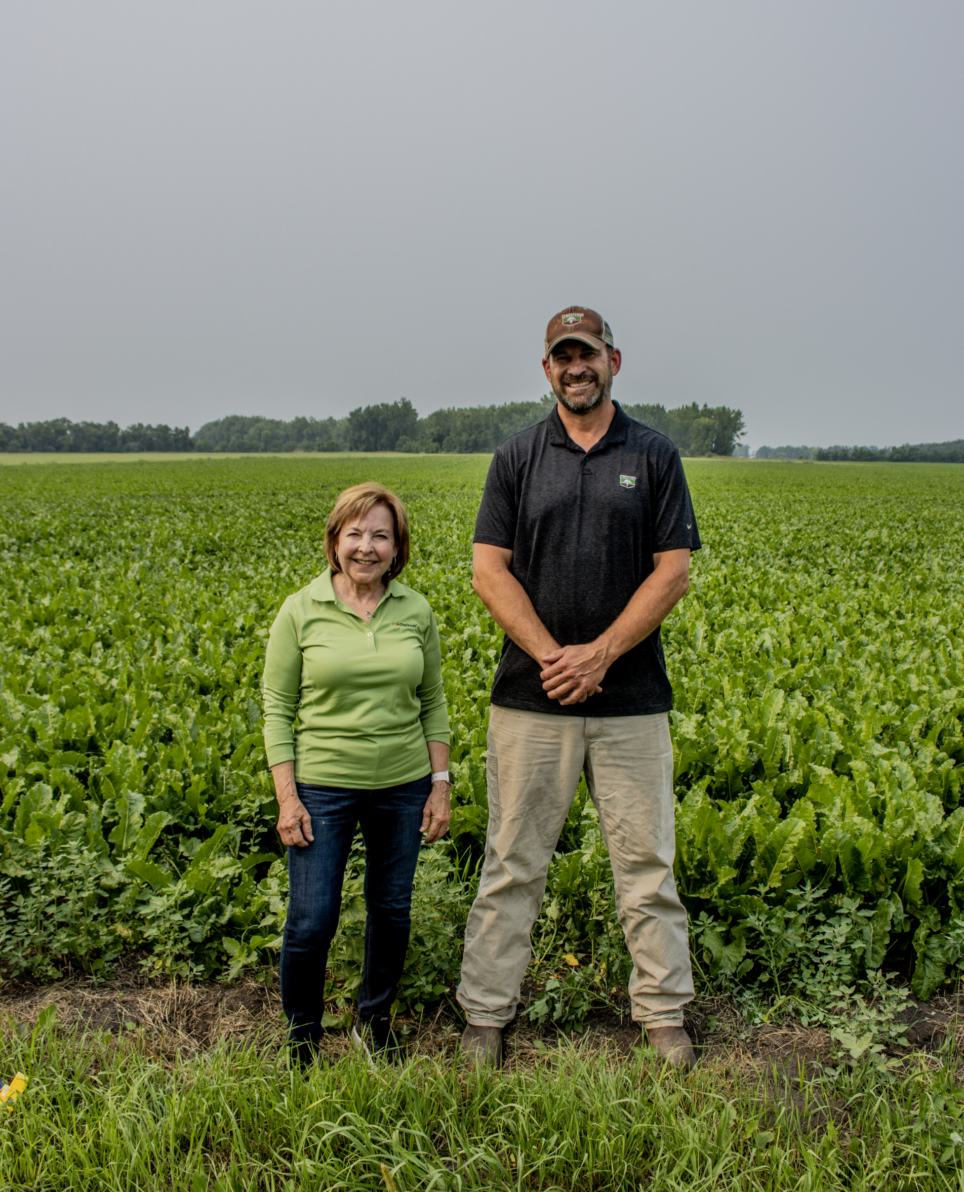 Two people standing in a green crop field under an overcast sky